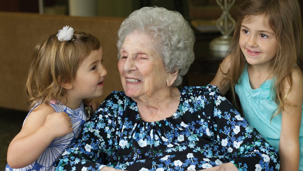 Elderly woman in wheelchair receiving kisses from her granddaughters at Manoogian Manor.