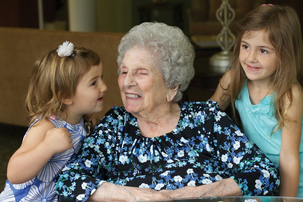 Elderly woman in wheelchair receiving kisses from her granddaughters at Manoogian Manor.