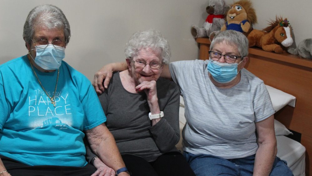 A senior female resident and her children sitting on a bed smiling.