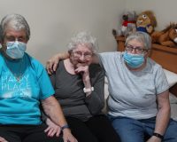 A senior female resident and her children sitting on a bed smiling.
