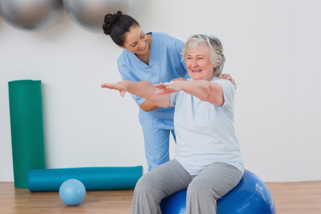 Senior woman sitting on exercise ball with physical therapist