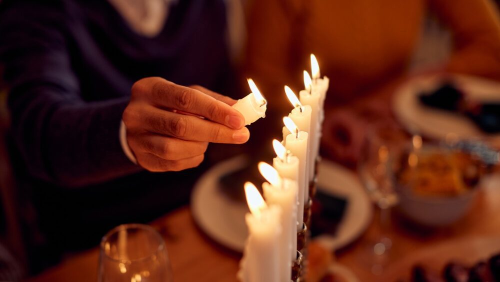 Close-up of Jewish man lightning the menorah during family dinner at dining table on Hanukkah.