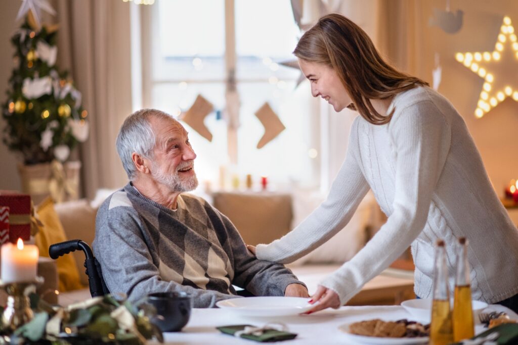 Young woman with senior in wheelchair indoors at home at Christmas, at the table.
