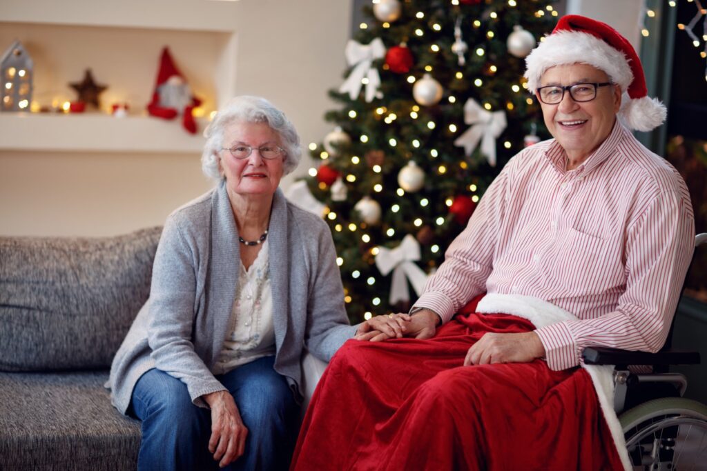 portrait of happy senior man in wheelchair and smiling woman with Christmas gift