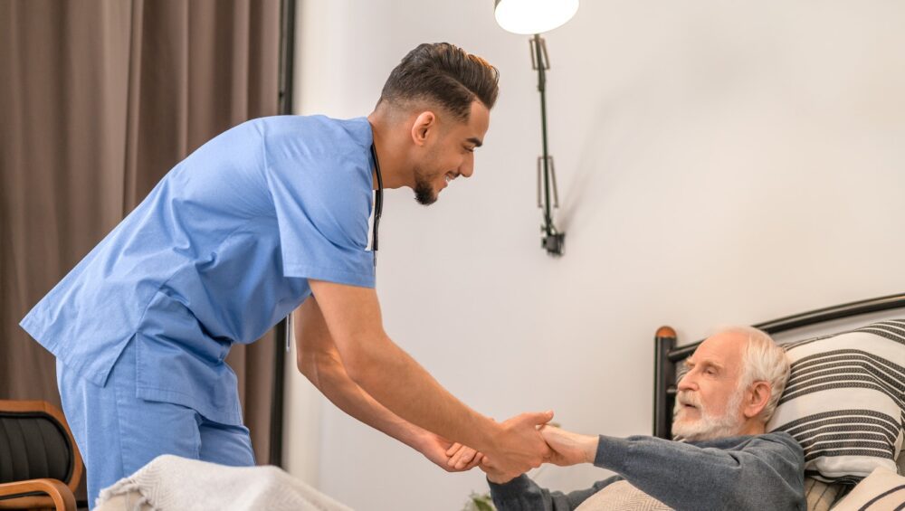 Smiling medical worker lifting a senior man from the bed