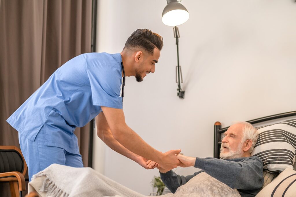 Smiling medical worker lifting a senior man from the bed