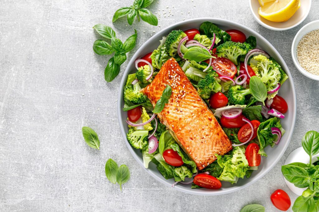 Grilled salmon fish fillet and fresh green leafy vegetable salad with tomatoes, and broccoli. Healthy food. Good for eye health.. Top view