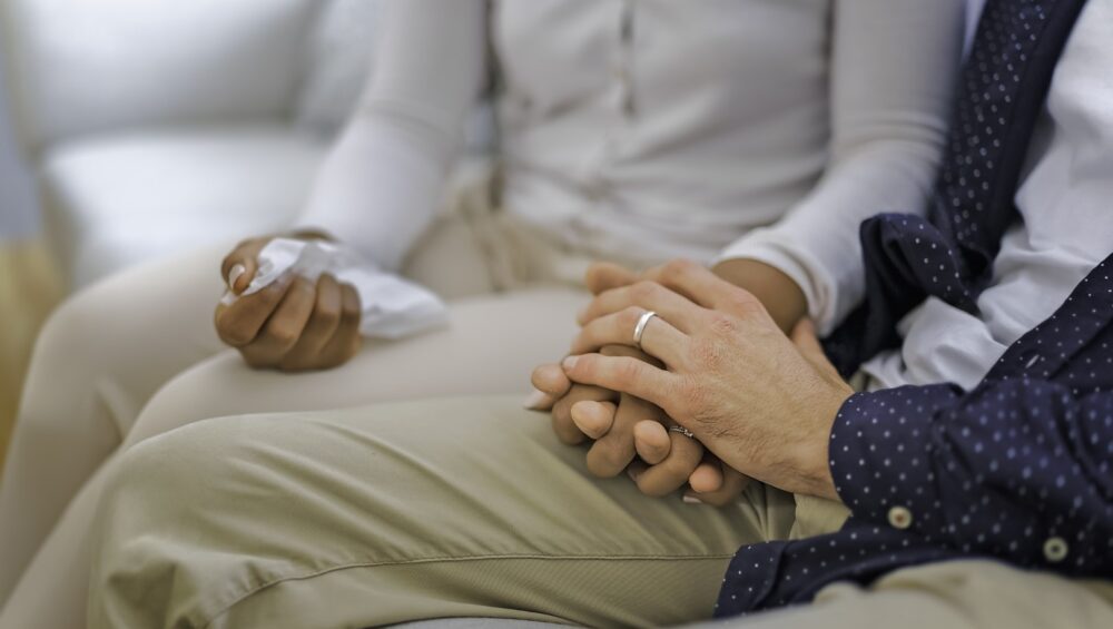 Senior couple holding hands and talking while sitting on couch