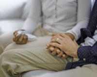 Senior couple holding hands and talking while sitting on couch