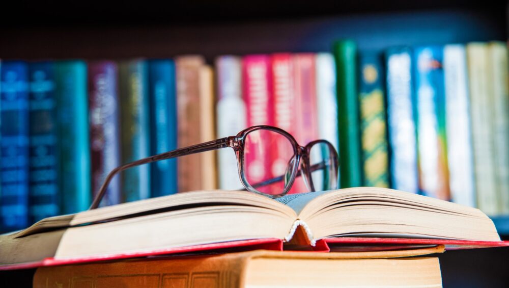 A pair of glasses sitting on a couple of books with books in the background