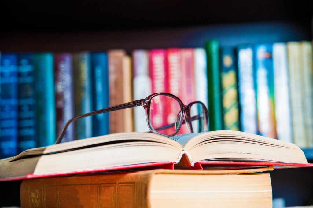 A pair of glasses sitting on a couple of books with books in the background