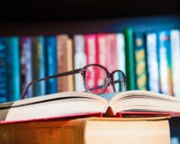 A pair of glasses sitting on a couple of books with books in the background