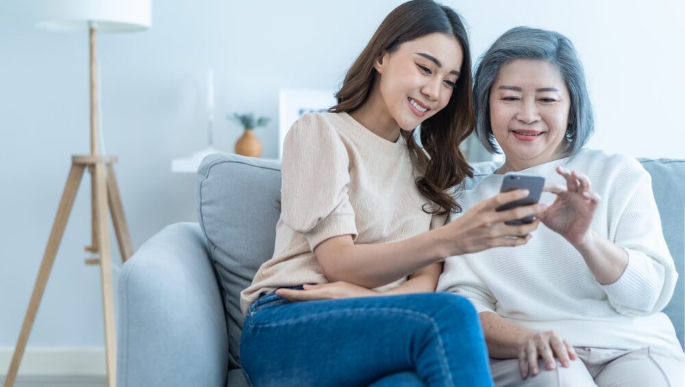 A young Asian woman helping an elderly Asian woman with her cellphone