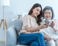 A young Asian woman helping an elderly Asian woman with her cellphone