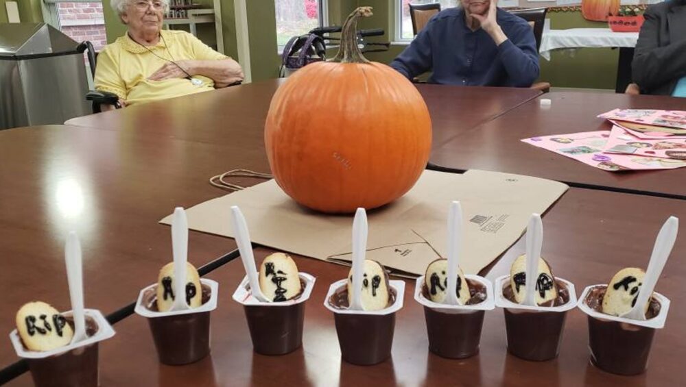 Close-up of Halloween desserts with a pumpkin in the middle of the table and senior citizens in the background.