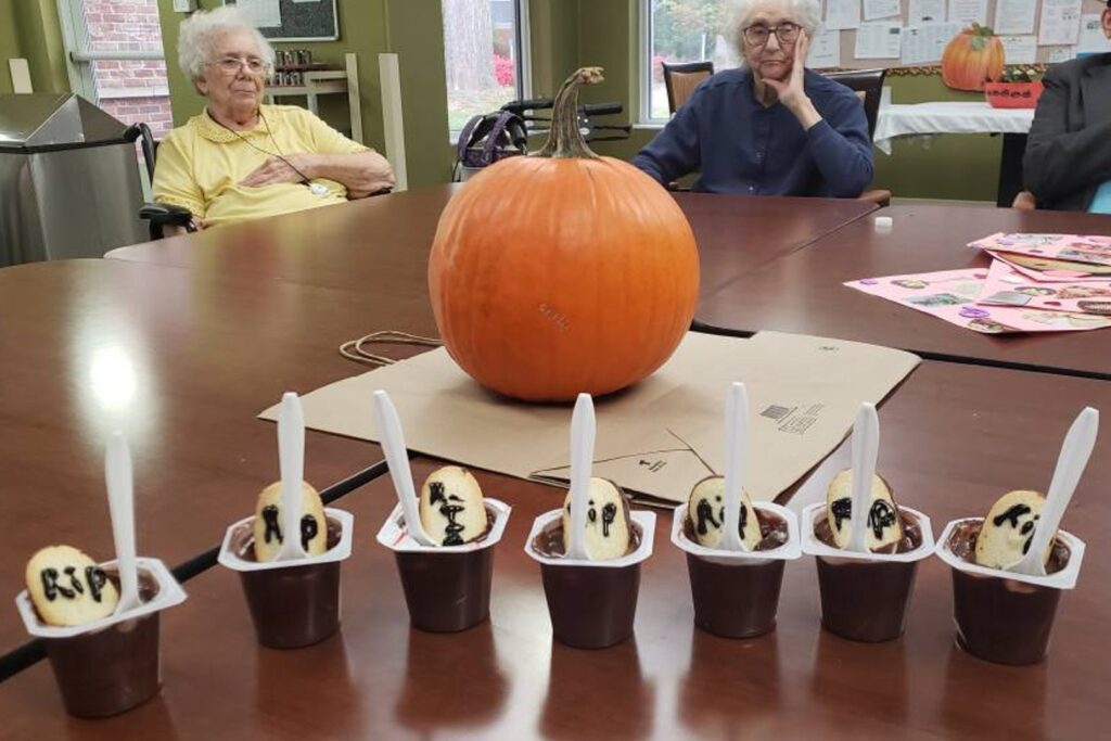 Close-up of Halloween desserts with a pumpkin in the middle of the table and senior citizens in the background.