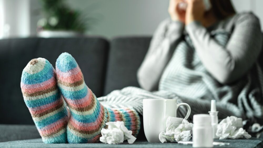 Woman sick with the flu blowing her nose surrounded by used tissues