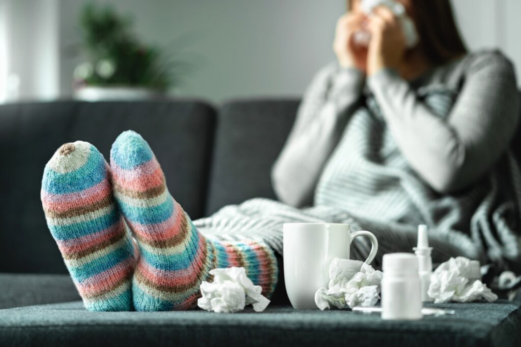 Woman sick with the flu blowing her nose surrounded by used tissues