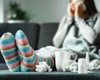 Woman sick with the flu blowing her nose surrounded by used tissues