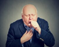 Old man coughing holding fist to mouth isolated on gray background