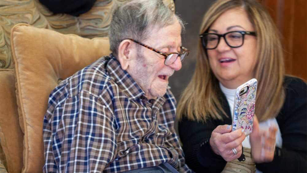 Elderly father at Manoogian Manor being shown photos on smartphone by family