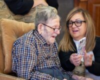 Elderly father at Manoogian Manor being shown photos on smartphone by family