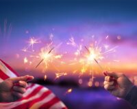 USA Celebration With Hands Holding Sparklers And American Flag At Sunset With Fireworks