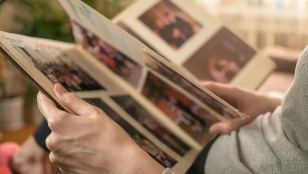 Woman flipping through a photo album filled with candid family and event pictures in a cozy, softly lit room.