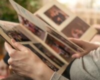 Woman flipping through a photo album filled with candid family and event pictures in a cozy, softly lit room.