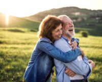 Happy senior couple outside in spring nature, hugging at sunset. Side view.